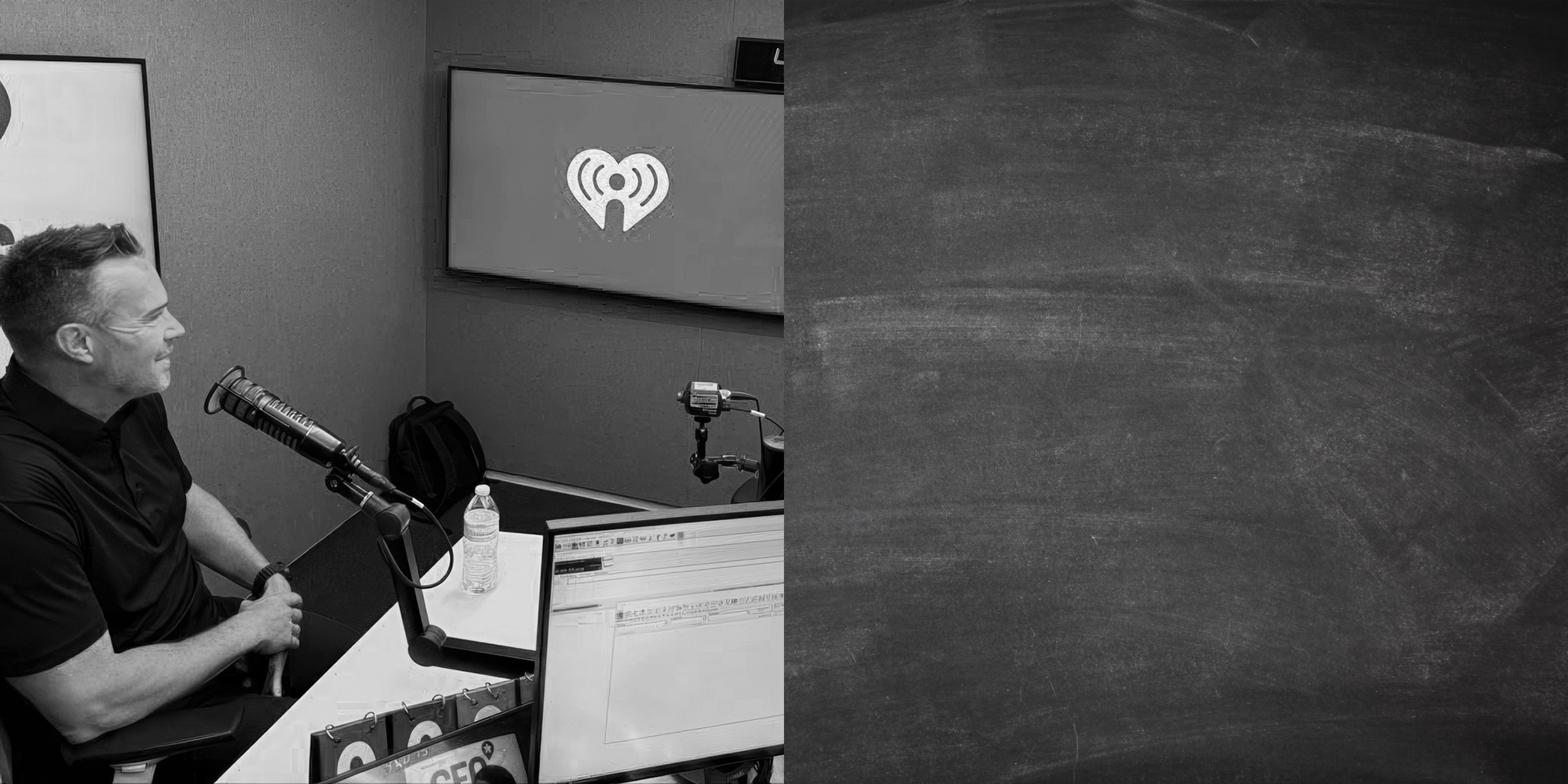 Black and white image of a man sitting in a radio studio with a microphone, water bottle, and multiple computer screens.